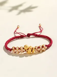 Détail d'un bracelet en corde rouge fait main avec serpent doré et nœuds de fleur de pêcher