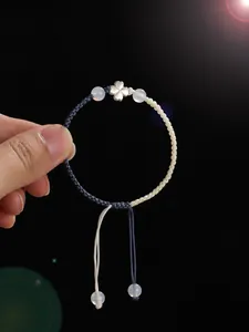 Détail d'un bracelet tissé main avec trèfle en argent 925 et perles d'agate blanche.