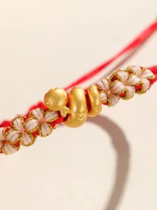 Détail d'un bracelet en corde rouge fait main avec un charme de serpent doré
