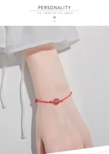 Detailed view of hand-woven red rope bracelet with strawberry crystal bead