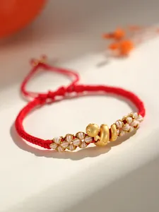 Gros plan d'un bracelet tressé rouge avec breloque serpent dorée et nœuds fleur de pêcher.