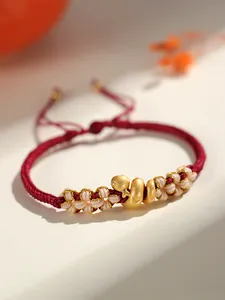 Détail d'un bracelet tressé rouge avec un charm de serpent doré et des nœuds de fleurs