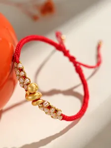 Gros plan d'un bracelet tressé rouge pour l'année du serpent avec des breloques dorées.