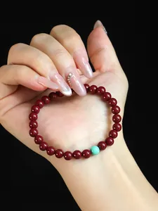 Detail of a red cinnabar bead bracelet with a single turquoise stone on a hand.