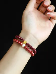 Detail shot of natural red cinnabar beaded bracelet with pearl worn on woman's wrist