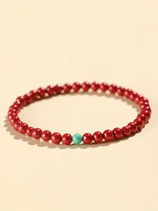 Detailed macro shot of a red cinnabar beaded bracelet featuring a single turquoise accent bead
