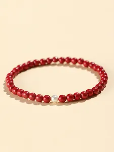 Close-up macro view of a red cinnabar beaded bracelet with a single white pearl detail.