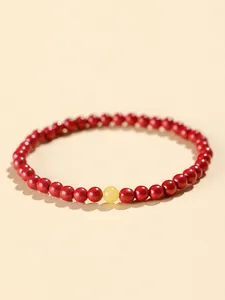 Detail view of a cinnabar beaded bracelet with small red beads and one yellow accent bead.
