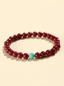 Macro detail shot of red cinnabar bead bracelet with a single turquoise accent bead.