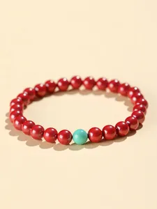 Detail shot of a red cinnabar bead bracelet with a turquoise bead on cream background