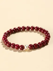 Detail of dark red cinnabar bead bracelet featuring a single white freshwater pearl.