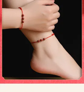 Détail du bracelet et de la chevillère en fil rouge cinabre et perles dorées sur peau