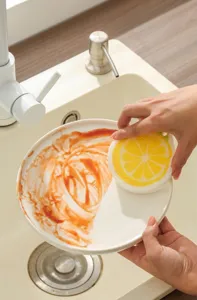 Gros plan d'une éponge en coton de pâte de bois en forme de citron nettoyant une assiette