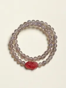 Gros plan d'un bracelet double rang en perles d'agate grise avec une perle rouge sculptée