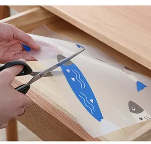 Detail of waterproof kitchen drawer mat being trimmed with scissors in a wooden drawer