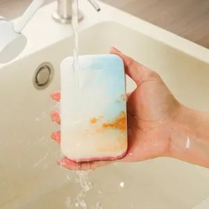 Tweezijdige keukenreinigingsspons die onder een waterkraan in een gootsteen wordt afgespoeld.