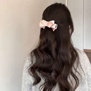 Detailed back view of a woman wearing a elegant pink satin bow hair clip on long wavy hair