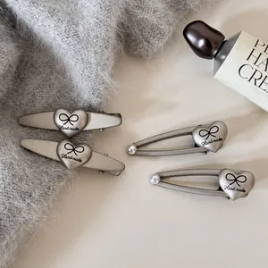 Vista detallada de pinzas para el cabello plateadas con forma de corazón y lazo.