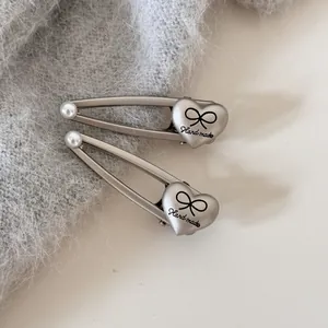 Primer plano de pinza para el pelo triangular plateada con perla y detalle de corazón