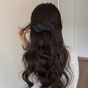 Elegant black satin bow hair clip shown on a wavy half-up ponytail style for women