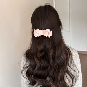 Close-up of a pink satin bow banana clip holding long wavy hair in a ponytail style