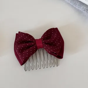 Close-up detail of burgundy polka dot bow hair comb with silver metal teeth for styling.