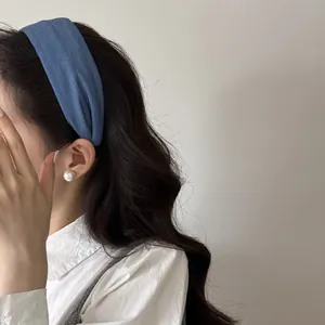 Dettaglio laterale di un cerchietto largo in tessuto blu denim su modella