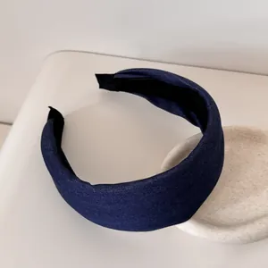 Vista dettagliata di un cerchietto largo in denim blu scuro su un vassoio bianco minimalista