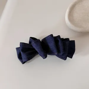 Dettaglio di un fermaglio per capelli in denim a pieghe con cuciture su sfondo neutro.