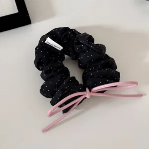 Detail view of a stylish black polka dot scrunchie with a pink leather bow tie