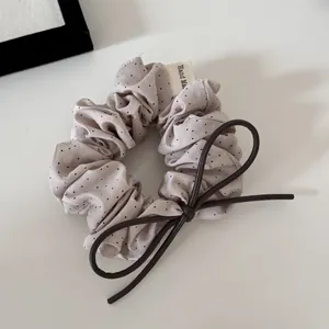 Close-up of polka dot scrunchie with brown leather bow and fabric Hand Made tag