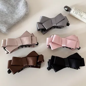 Detailed view of multiple satin bow banana hair clips in pink, grey, and brown colors