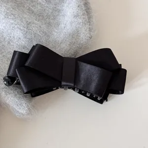 Close-up of a elegant black satin bow banana hair clip resting on soft grey fabric