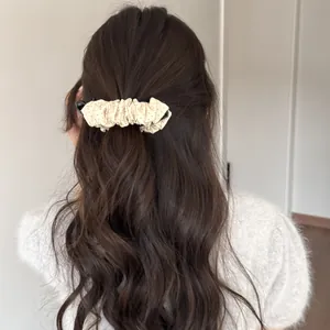 Vue détaillée d'une barrette banane plissée à pois beige fixant une queue de cheval.