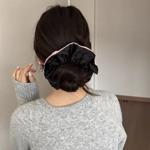 Detailed view of an oversized black scrunchie with pink edges on a woman's hair bun