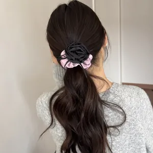 Detailed view of an elegant black fabric rose hair scrunchie on a wavy brown ponytail
