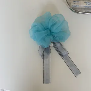 Close-up detail of a blue organza flower scrunchie with pearl charm and grey ribbons.