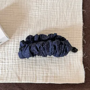 Gros plan sur la texture du tissu à pois bleu marine de la pince à cheveux banane plissée