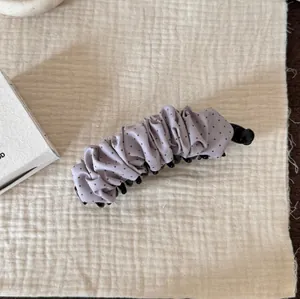 Gros plan d'une pince banane en tissu froncé à pois violets sur un fond texturé beige.