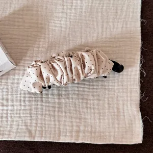 Vue détaillée d'une pince à cheveux banane à pois beige sur un fond de tissu texturé