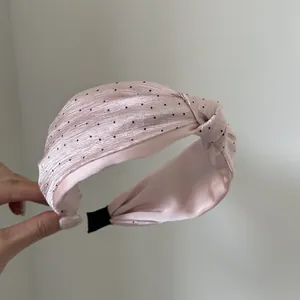 Primo piano di un cerchietto rosa a pois con nodo e trama elegante in raso setoso.