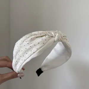 Dettaglio di un cerchietto bianco annodato con pois neri e finitura lucida satinata