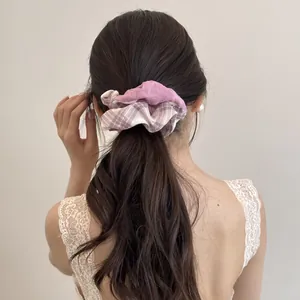 Detailed view of a purple and plaid fabric scrunchie styled in a low ponytail on wavy hair