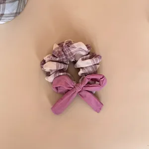 Macro detail view of a checkered plaid hair scrunchie featuring a purple fabric bow accent