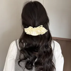 Détail de la pince à cheveux noeud plissé crème avec strass sur de longs cheveux bouclés