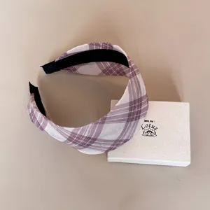 Detail view of a purple and white plaid wide headband resting on a white gift box