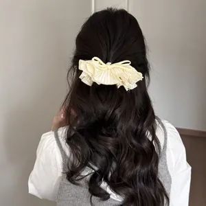 Vue arrière d'une élégante barrette à nœud plissé crème avec strass sur cheveux noirs
