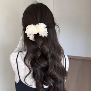 Detalle de una pinza para el pelo tipo banana con flores de malla plisada en pelo ondulado