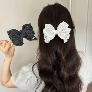 Elegant black and white polka dot bow hair clip shown on a model with long wavy hair