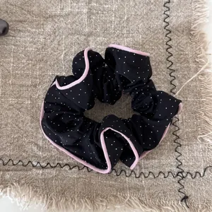 Macro detail of a black polka dot scrunchie with pink wood ear edge on linen background